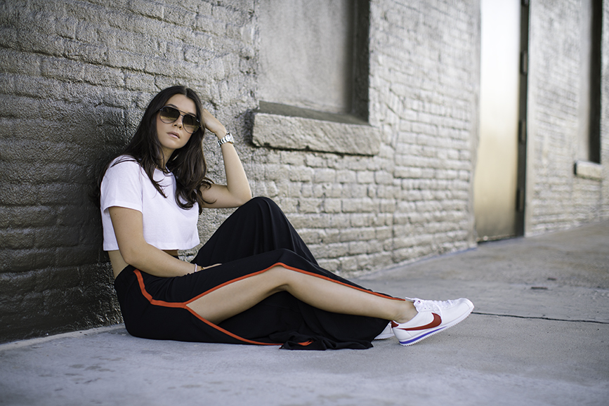Liv sitting wearing Nike Cortez, Forever 21 palazzo track pants, cropped t-shirt and quay sunglasses