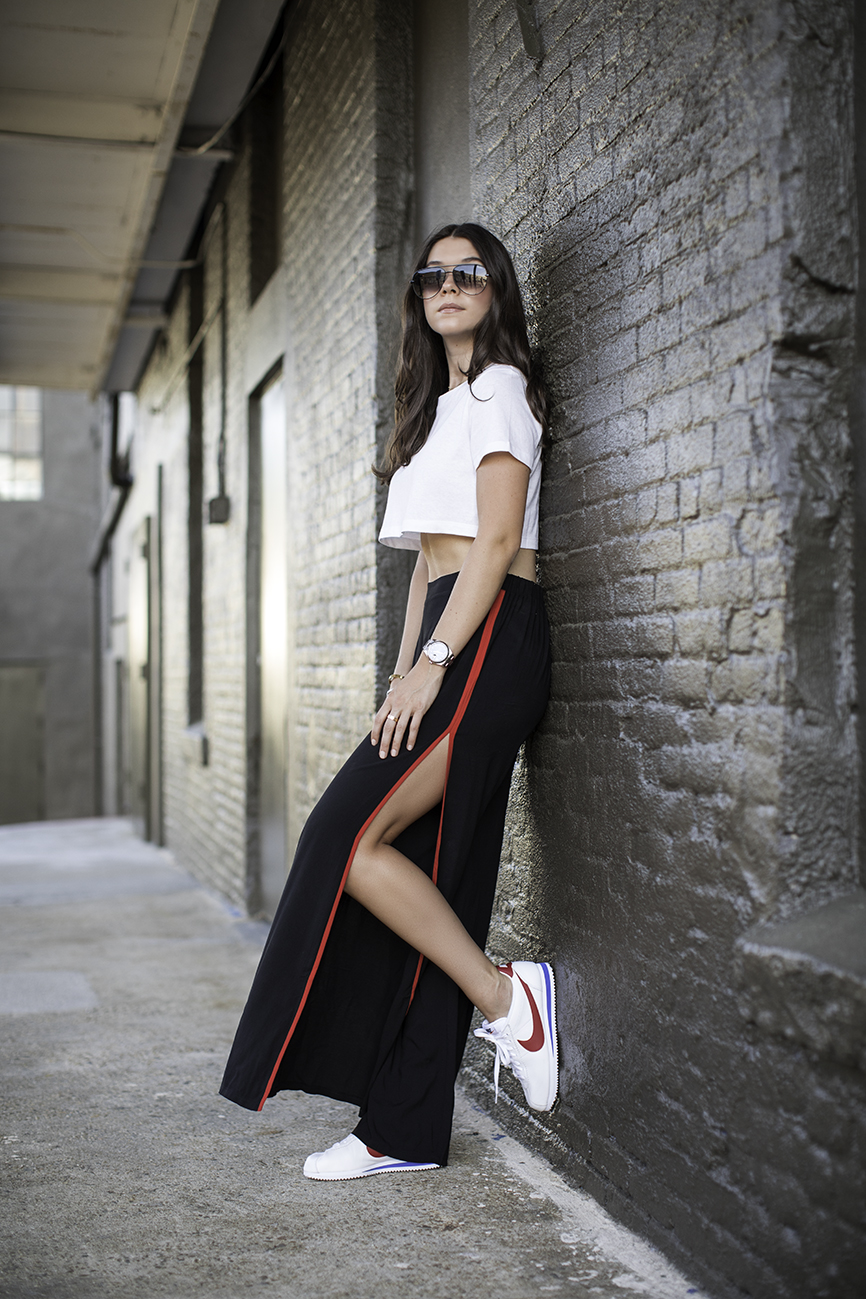 Liv against a wall wearing Nike Cortez, Forever 21 black red palazzo track pants, cropped t-shirt and quay sunglasses