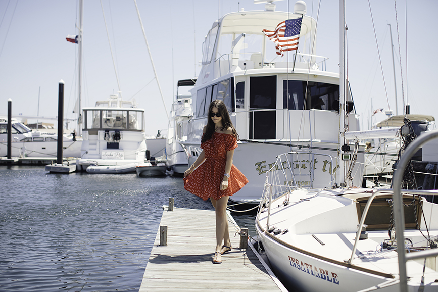 Liv walking on a dock in Newport Rhode Island just steps away from the Newport Marriott wearing an off the shoulder dress by Faithful the Brand. 