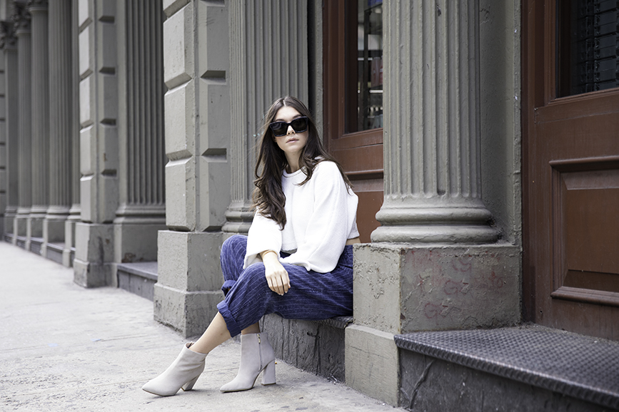 Liv Micheli sitting in SoHo wearing OFF WHITE c/o Virgil Abloh x Warby Parker Medium sunglasses, Urban Outfitters Roll neck Cropped Sweater, Silence + NoiseRelaxed-Fit trousers and Kenneth Cole boots.
