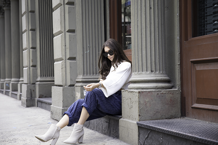 Liv Micheli sitting in SoHo wearing OFF WHITE c/o Virgil Abloh x Warby Parker Medium sunglasses, Urban Outfitters Roll neck Cropped Sweater, Silence + Noise Relaxed-Fit trousers and Kenneth Cole boots.