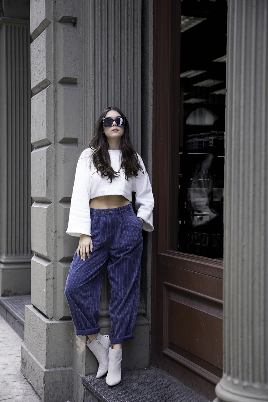 Liv Micheli standing in the streets of SoHo wearing OFF WHITE c/o Virgil Abloh x Warby Parker Medium sunglasses, Urban Outfitters Roll Kneck Cropped Sweater, Silence + Noise Relaxed-Fit trousers and Kenneth Cole boots.