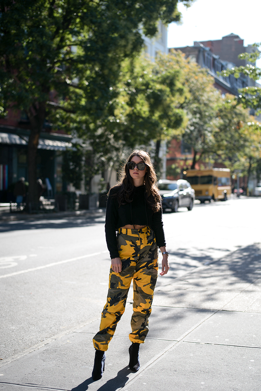 Liv Micheli is in the streets of Soho, New York wearing a Danielle Guizio hoodie, Rothco Stinger Yellow Camo Pants, Public Desire Boots and Off-White c/o Virgil Abloh x Warby Parker Sunglasses