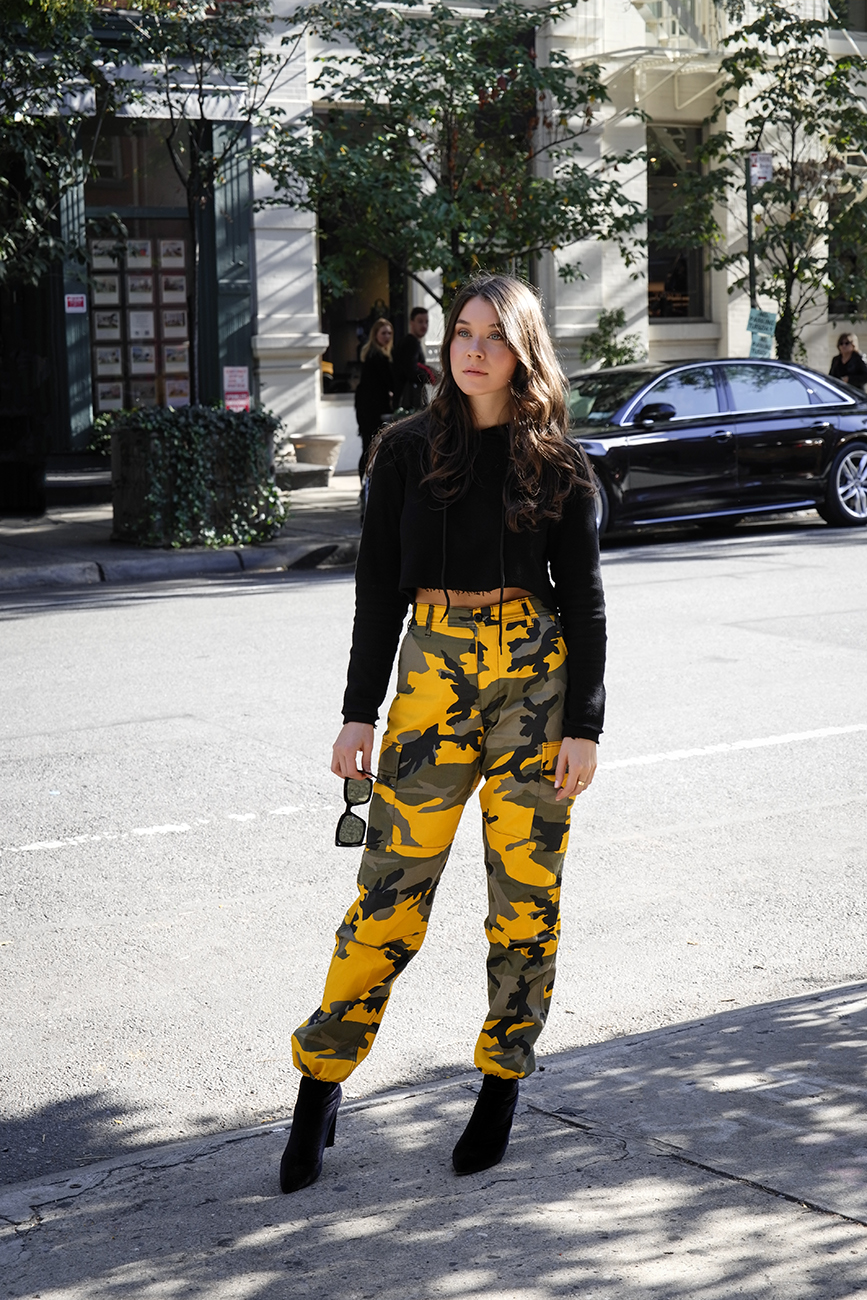 Liv Micheli is in the streets of Soho, New York wearing a Danielle Guizio hoodie, Rothco Stinger Yellow Camo Pants, Public Desire Boots and Off-White c/o Virgil Abloh x Warby Parker Sunglasses