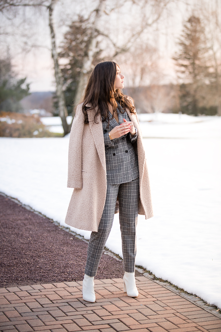 Blogger and Influencer, Liv Micheli, is wearing the SUISTUDIO Cameron Grey Checked Suit, the Light Brown Overcoat and Stuart Weitzman Clinger Boots in white leather at Westchester Country Club