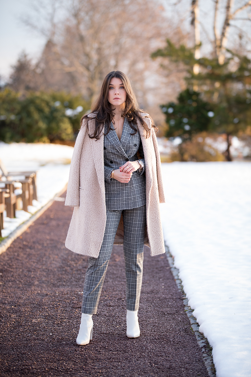 Blogger and Influencer, Liv Micheli, is wearing the SUISTUDIO Cameron Grey Checked Suit, the Light Brown Overcoat and Stuart Weitzman Clinger Boots in white leather at Westchester Country Club
